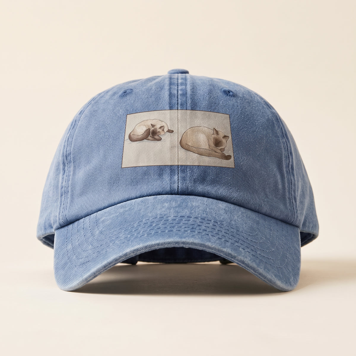 Two Siamese cats asleep side by side in watercolor, printed in a framed panel on the front of a Blue Jean washed cap (mockup)