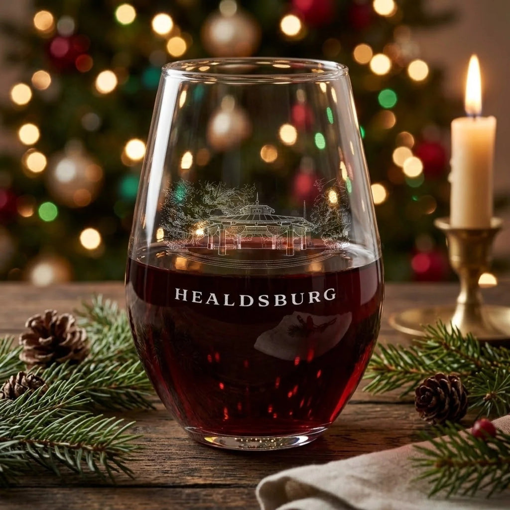 Healdsburg Plaza gazebo engraved stemless wine glass with red wine on a holiday table, with candlelight, evergreen and pine cones